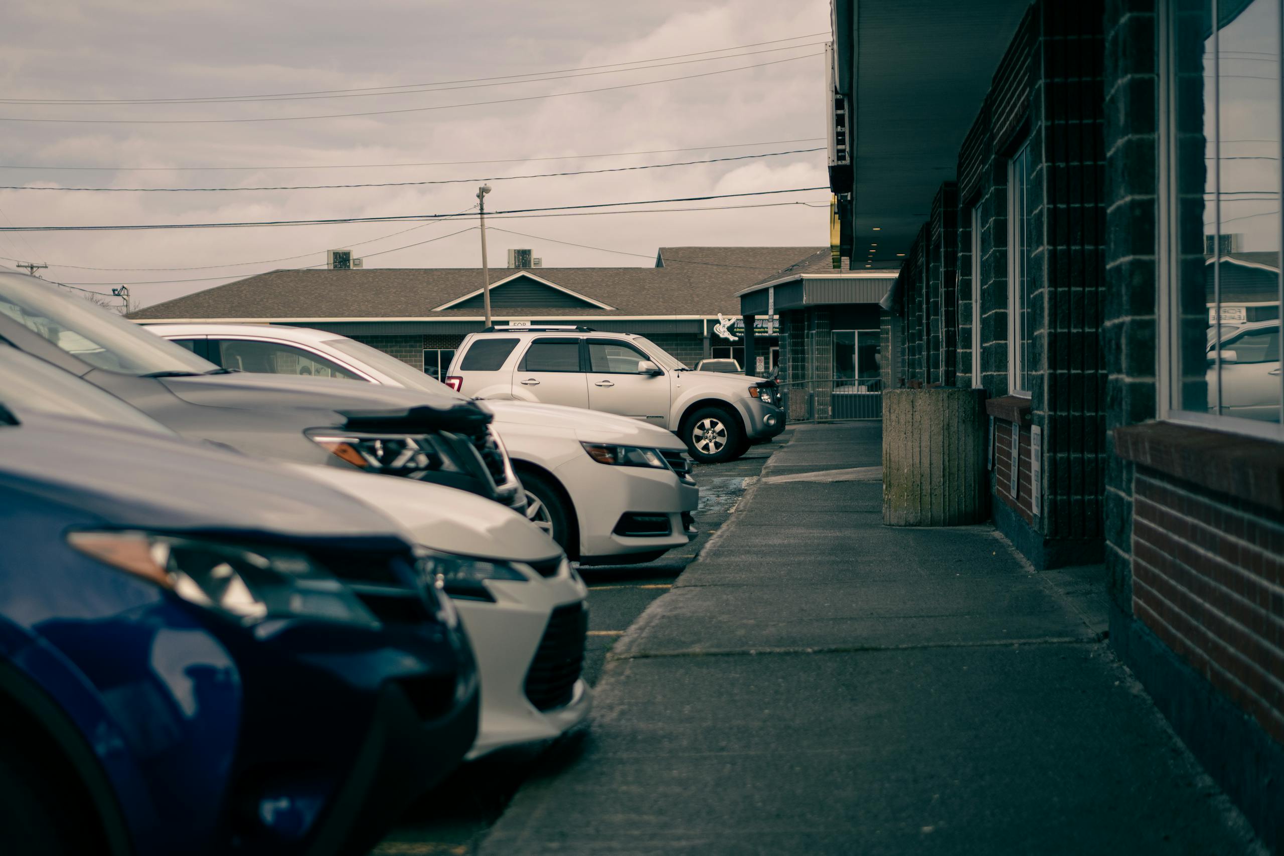 Row of parked SUVs outside urban buildings under cloudy skies.